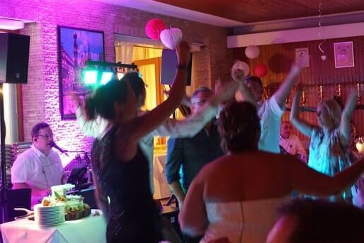 Gäste tanzen ausgelassen auf einer Hochzeitsfeier, während ein Live-Musiker im Hintergrund für Stimmung sorgt