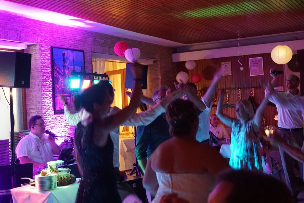 Tanzende Gäste mit erhobenen Armen bei Hochzeitsfeier mit Live-Musik
